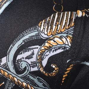 Detailed macro view of black baseball cap fabric featuring golden chain and blue baroque patterns
