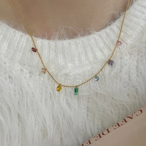 Detail of 14K gold-plated necklace with colorful zircon pendants on white knitwear