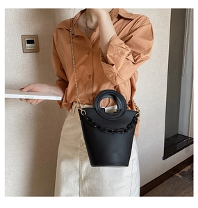 Detail of black bucket bag featuring round cutout handle and decorative chunky black chain