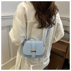 Close-up of light blue leather crossbody bag featuring a golden H-shaped metal buckle