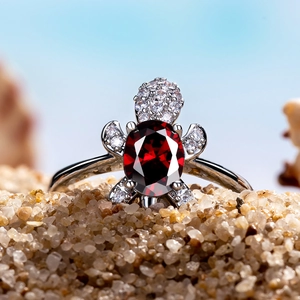 Macro view of turtle ring with red ruby gemstone set in white gold on beach sand