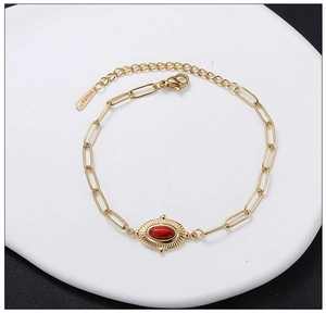 Close-up of gold paperclip bracelet with red stone and S-STEEL tag detail