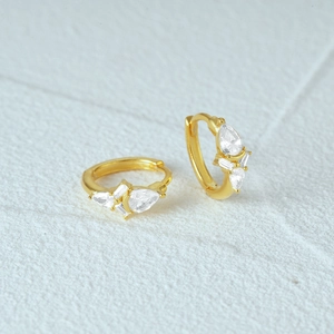 Macro detail of gold-plated silver huggie earrings with drop and rectangle clear zircons