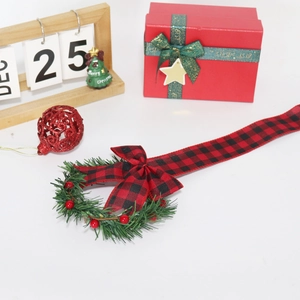 Close-up of artificial pine wreath with red berries and buffalo plaid bow on white background