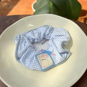 Close-up of a light blue plaid scrunchie with a unique NOTES tag on a wooden table