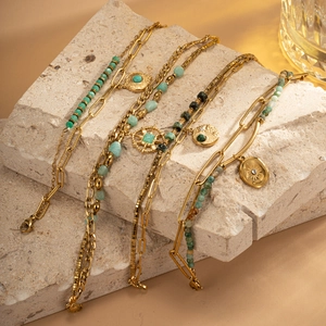 Detail of bohemian gold-tone chain bracelets with green natural stone and sun charms