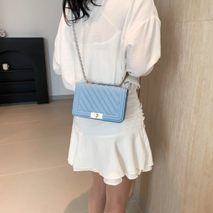 Detailed view of sky blue quilted crossbody bag with metal chain strap worn by a model