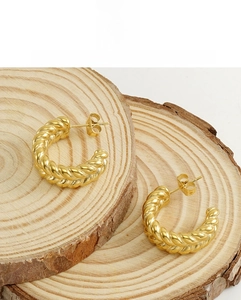 Detail view of gold C-shaped twisted earrings with wheat texture on a rustic wood surface