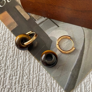 Détail de boucles d'oreilles créoles avec perles d'oeil de tigre sur fond rustique