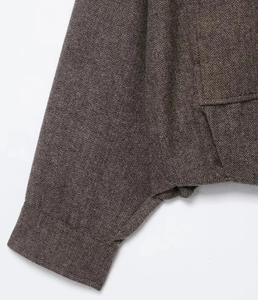Close-up of brown herringbone tweed fabric showing detailed stitching on pocket and cuff