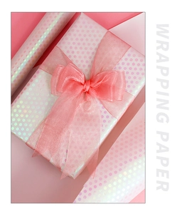 Close-up of pink iridescent polka dot wrapping paper with a matching chiffon ribbon bow