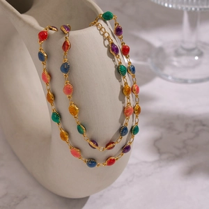 Detail showing gold necklace with colorful enamel shell charms on a white vase