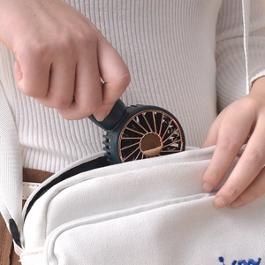 Portable dark green mini USB fan with gold grille being placed in a canvas bag pocket
