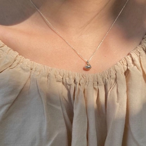 Detailed view of a minimalist silver bean pendant necklace worn by a model in sunlight