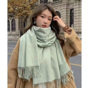 Thick mint green cashmere-like scarf with fringe on model in a stylish outdoor street view