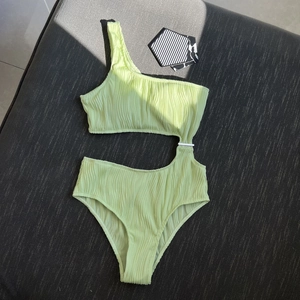 Detail of lime green one-shoulder swimsuit with side cutout and textured fabric