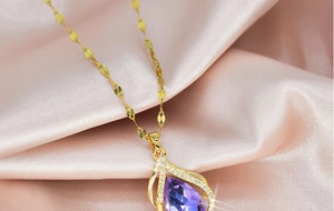 Close-up of gold water drop necklace with purple gemstone on pink silk fabric
