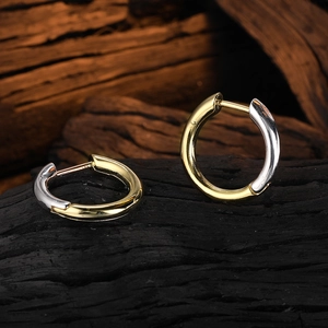 Macro shot of two-tone hoop earrings with gold and silver finish on charred wood base