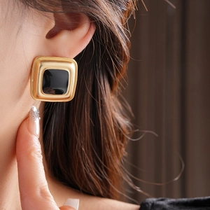 Close-up of vintage gold earrings with black square enamel stones on a professional model