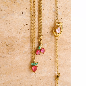 Detailed macro view of cherry, strawberry, and planet gold necklaces on marble base