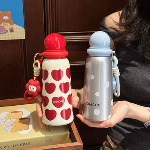 Close-up of cute stainless steel thermos with red heart and flower charm on a tray
