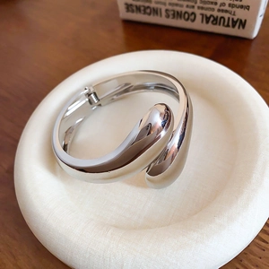 Dettaglio del bracciale rigido in argento lucido con design a goccia in metallo fluido