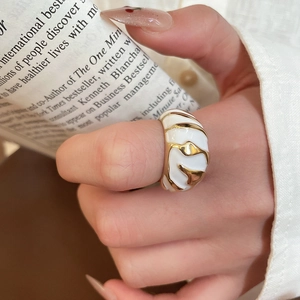 Macro shot of gold croissant ring with white enamel waves on vintage paper