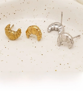 Macro shot of gold and silver croissant earrings with brushed metal texture