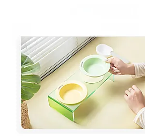 Dual ceramic pet feeding station with acrylic stand and hand placing yellow bowl