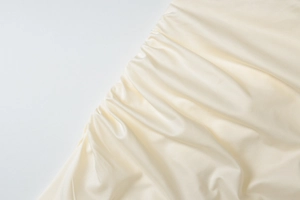 Detailed macro view of off-white satin fabric with elegant side pleats and ruched texture