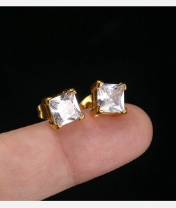 Detailed view of 18K gold square zircon earrings with claw setting held on a fingertip