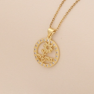 Detail of a gold mama heart pendant necklace with shimmering zircon accents on beige linen