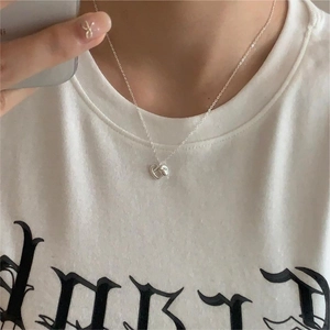 Close-up of a minimalist silver heart pendant necklace worn on a white graphic t-shirt