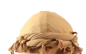 Close-up of khaki turban with intricate braided details and tassel decoration on white background