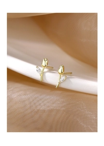 Close-up of gold tulip stud earrings featuring a clear gemstone on champagne fabric