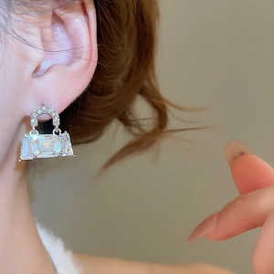 Close-up of sparkling cubic zirconia paved handbag-shaped stud earring on model ear