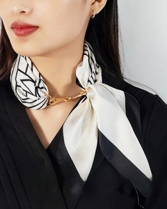 Close-up of golden horsebit scarf ring on a patterned silk scarf worn by a model