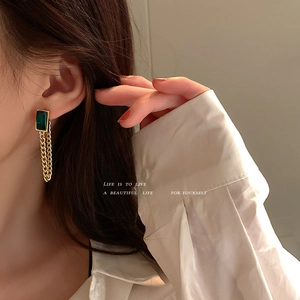 Close-up of model wearing emerald glass tassel earrings with elegant gold metal chains