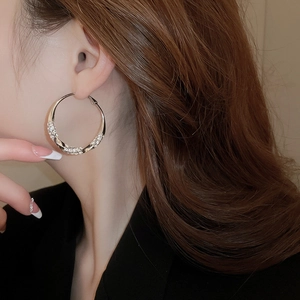 Close-up of a model wearing a large silver-tone twisted hoop earring with sparkling pavé crystals