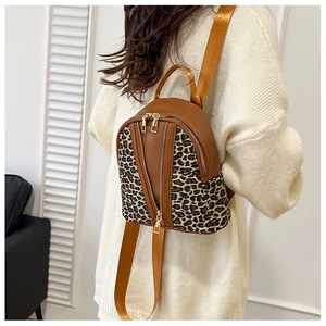Detail view of a small leopard print backpack worn over a white sweater in a casual style