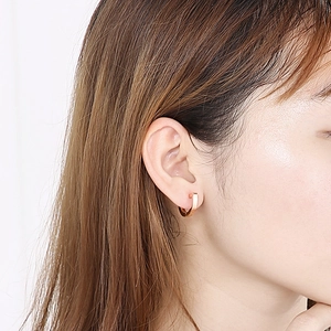 Close-up of rose gold D-shaped geometric hoop earrings worn by a model on a white backdrop