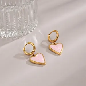 Golden heart earrings with pink marbled enamel drops on a textured glass backdrop