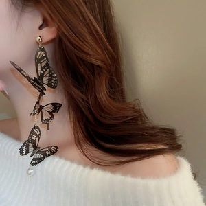 Détail de boucles d'oreilles papillon noir avec franges et pendentif en perle blanche