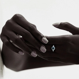 Close-up of a silver ring with a blue gemstone and halo diamonds on a model's hand