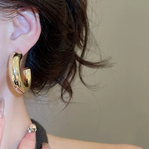 Close-up of a model wearing high-polished chunky gold C-shaped hoop earrings