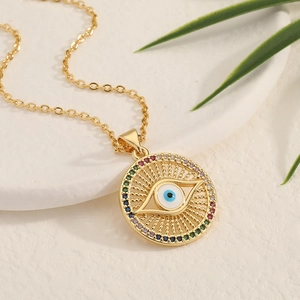 Golden necklace with a zircon-encrusted Evil Eye pendant on a white marble background