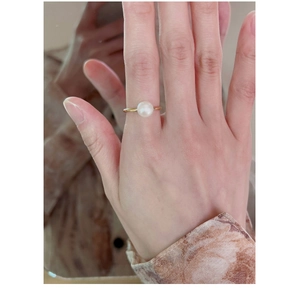 Close-up of a delicate golden pearl ring on a model's hand featuring a white round pearl