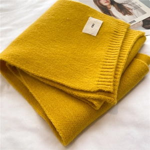 Detail of soft yellow knitted scarf with ribbed edge and owo logo tag on white bed