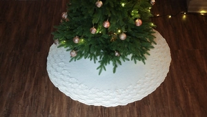 Close-up of cream knitted Christmas tree skirt on dark wood floor in festive home setting