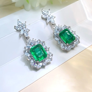 Luxurious emerald cut green gemstone drop earrings with sparkling diamond halo on white plate